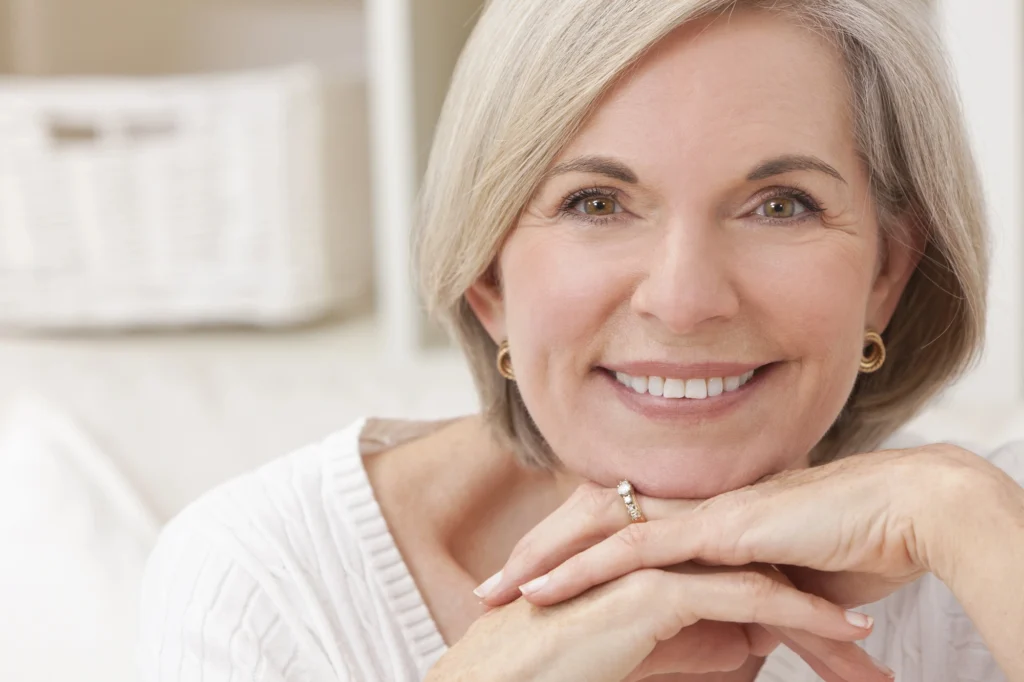 older woman smiling and resting her face on her hands after getting Invisalign in Cary, NC