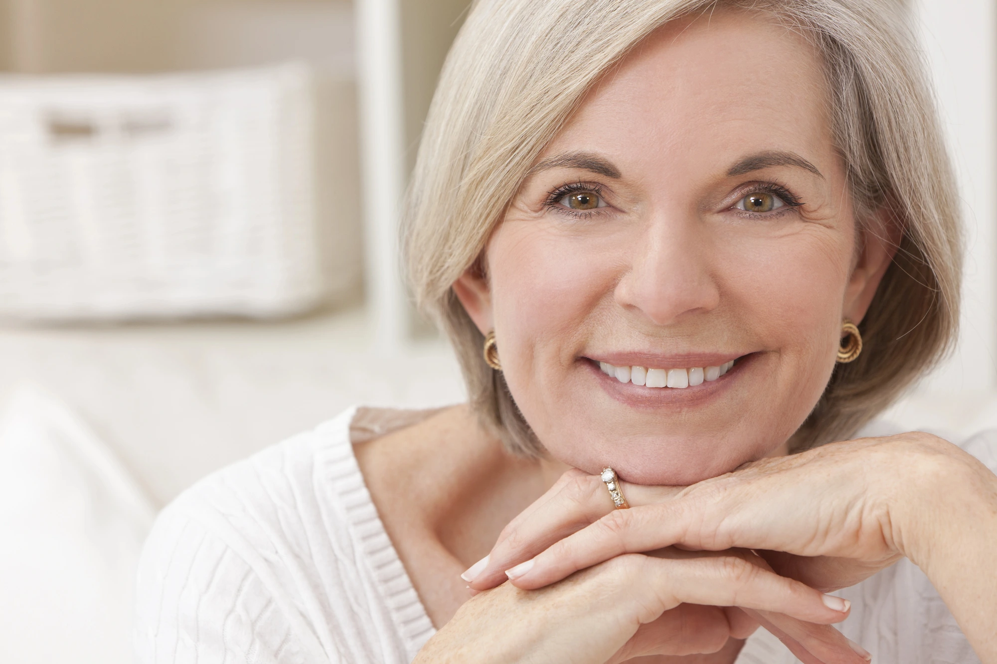 older woman smiling and resting her face on her hands after getting Invisalign in Cary, NC